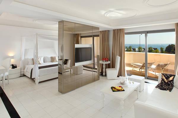 Modernes Hotelzimmer mit Meerblick, komplett in Weiß gehalten, mit einem großen Bett, Fernseher, und einer Terrasse.