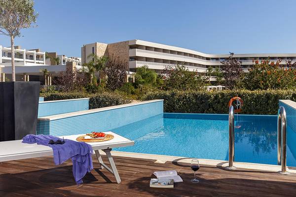 Poolbereich am Princess Andriana Resort & Spa mit Sonnenliegen, Weingläsern und einem Buch.
