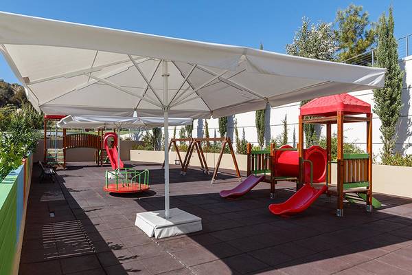 Kinderspielplatz im Freibereich des Princess Andriana Resort mit Rutschen und Spielgeräten unter einem großen Sonnenschirm.