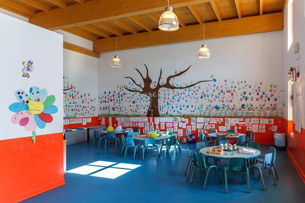 Innenansicht eines Kinderspielzimmers mit bunten Wandgestaltungen, Tischen und Stühlen.