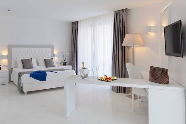 Ein modernes Zimmer im Princess Andriana Resort & Spa mit einem weißen Bett, Tisch, Lampe und Fernseher.