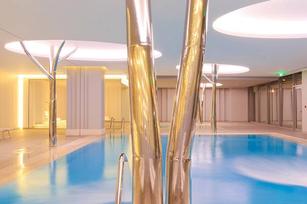 Innenpool des Princess Andriana Resort & Spa mit modernen goldenen Säulen und runden Deckenleuchten.