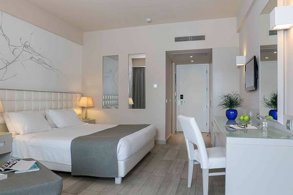 Hotelzimmer im Princess Andriana Resort & Spa mit weißem Bett, Nachttischen und Lampen.