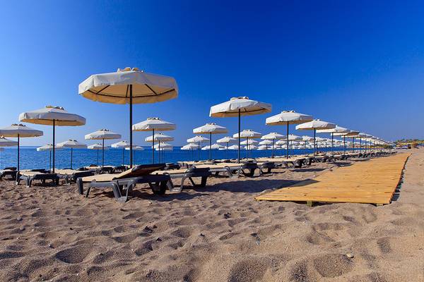 Strand des Princess Andriana Resort & Spa mit vielen Sonnenliegen und weißen Sonnenschirmen.