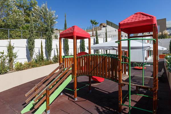 Kinderspielplatz im Princess Andriana Resort und Spa mit Holzspielgeräten und roten Dächern.