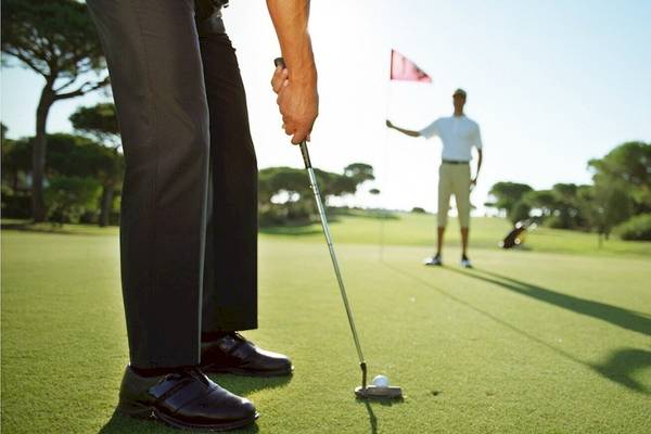 Golfer beim Putten auf einem Golfplatz mit grünem Rasen und Bäumen im Hintergrund.