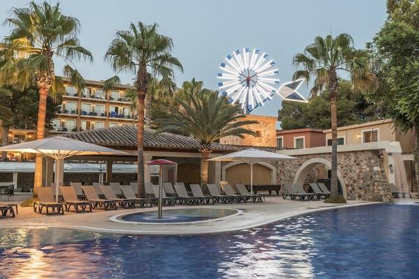 Außenbereich eines Hotels mit Pool, Loungeliegen, Schirmen und einem Karussell im Hintergrund.