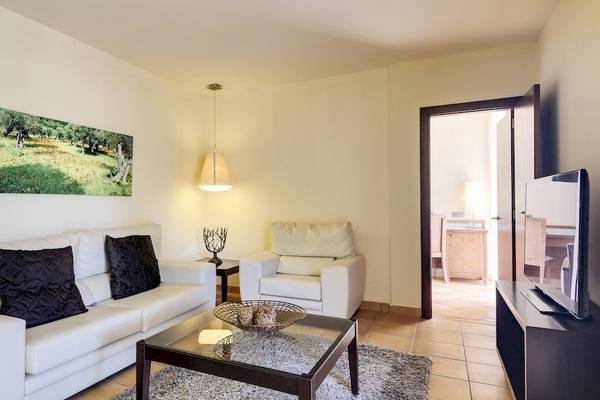 Wohnbereich eines Hotelzimmers mit weißer Couch, schwarzem Tisch und Fernseher.