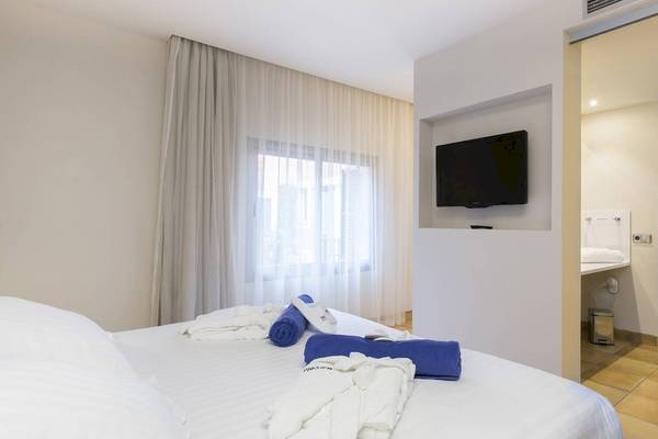 Ein modernes Zimmer im Occidental Playa de Palma mit einem Fernseher an der Wand und einem Bett mit weißen Laken.