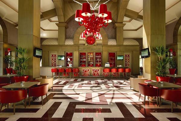 Innenansicht der Hotellobby des Cornelia Diamond Golf Resort & Spa mit rotem Kronleuchter, Tischen und Stühlen.