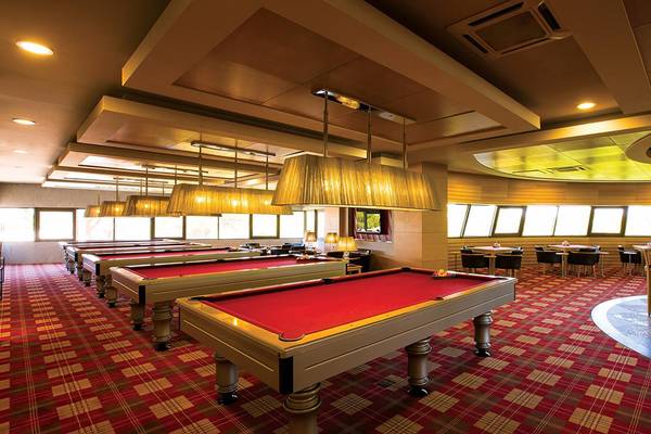 Innenansicht der Poolhalle im Cornelia Diamond Golf Resort & Spa mit roten Billardtischen und einem Barbereich.