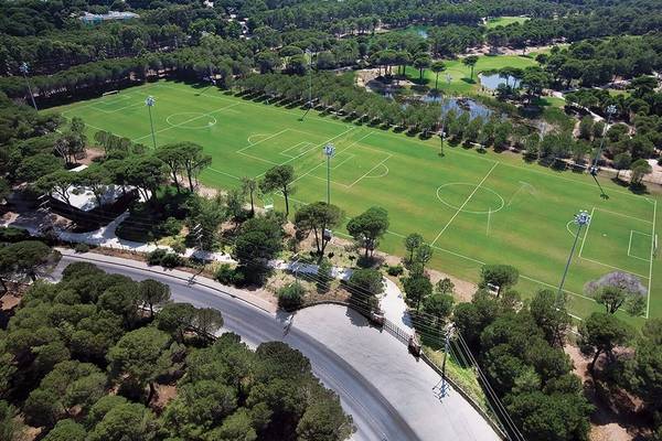 Luftaufnahme des Fußballplatzes im Cornelia Diamond Golf Resort & Spa mit umgebenden Bäumen und einer Straße.