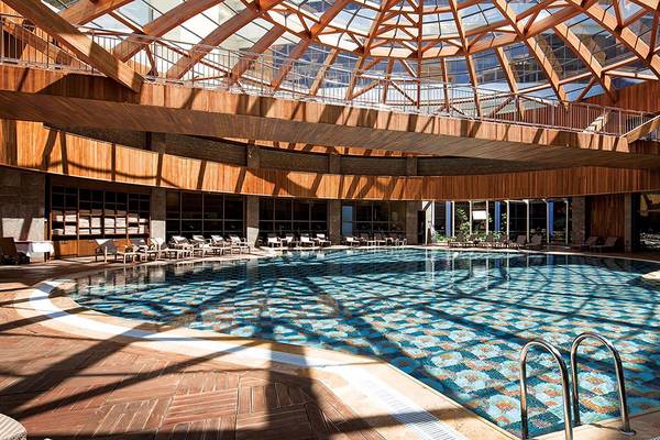 Innenpool im Cornelia Diamond Golf Resort & Spa mit einer Glaskuppel und Holzelementen.