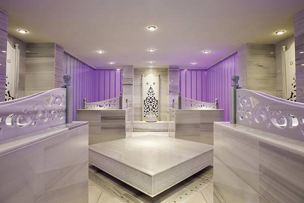 Innenbereich der Sauna im Cornelia Diamond Golf Resort & Spa mit violetten Vorhängen und weißen Marmorelementen.