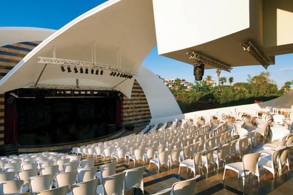 Außenansicht des Auditoriums des Cornelia Diamond Golf Resort & Spa mit vielen weißen Stühlen und einer Bühne.