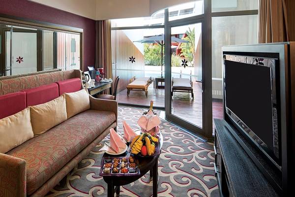 Wohnzimmer im Cornelia Diamond Golf Resort & Spa mit einem Sofa, einem Tisch mit Früchten, einem Fernseher und einer Terrasse mit Liegestühlen.