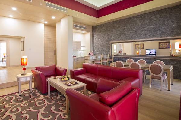 Das Wohnzimmer des Cornelia Diamond Golf Resort & Spa mit rotem Ledersofa, Esstisch und Fernseher.