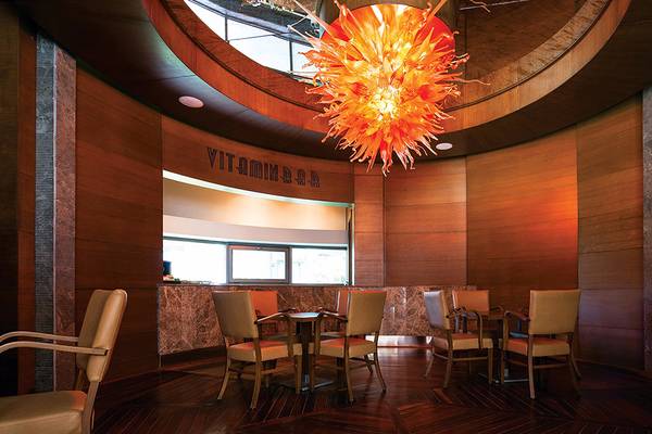 Innenansicht der Vitamin Bar im Cornelia Diamond Golf Resort & Spa mit Holzmöbeln und einer großen Glasleuchte.
