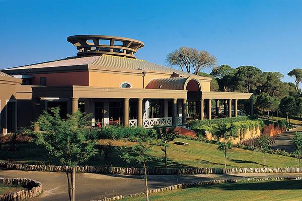 Außenansicht des Cornelia Diamond Golf Resort & Spa mit einer großen, runden Dachstruktur und umgeben von Bäumen und Rasen.