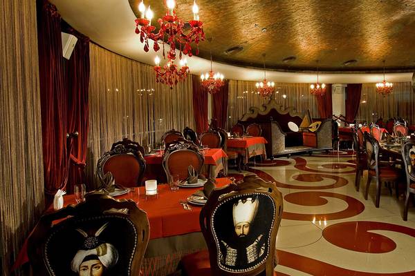 Restaurant-Innenbereich im Cornelia Diamond Golf Resort & Spa mit roten Tischdecken und goldenen Kronleuchtern.