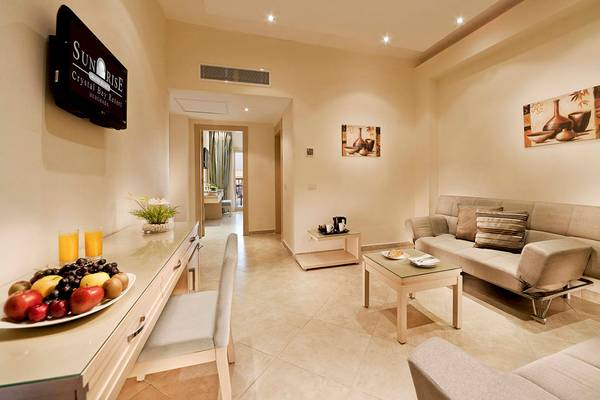 Suite Wohnbereich im Sunrise Crystal Bay Resort mit Fernseher, Sofa, Tisch und Obstteller.