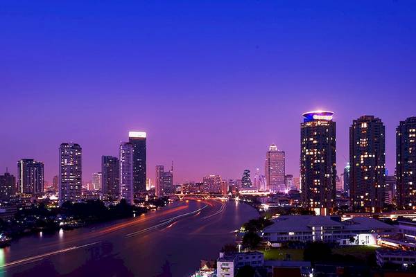 Abendliche Stadtansicht von Bangkok mit dem Chatrium Hotel Riverside, das sich am Flussufer befindet.