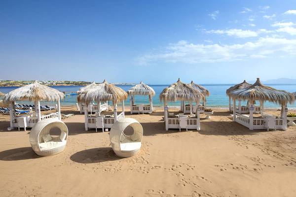 Strand des Sunrise Crystal Bay Resorts mit weißen Sonnenliegen und Strohdächern.