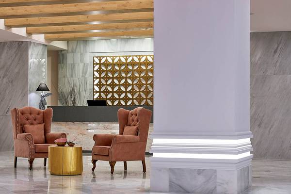 Innenansicht der Lobby des Mythos Palace Resort & Spa mit Marmorwänden, Holzdecke und braunen Sesseln.