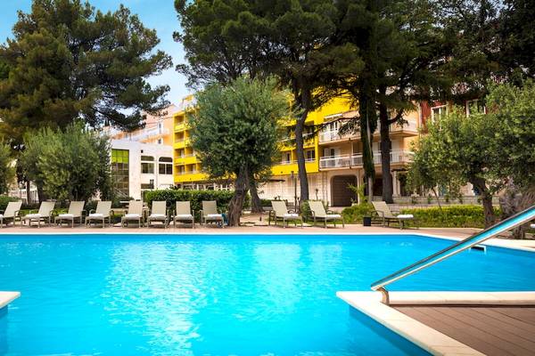 Außenpool des Remisens Hotel Epidaurus mit vielen Sonnenliegen und gelbem Gebäude im Hintergrund.