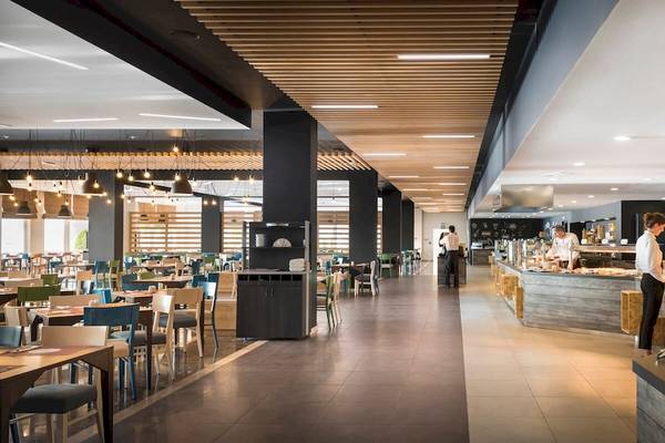 Innenansicht des Restaurants im Remisens Hotel Epidaurus mit Tischen, Stühlen und Angestellten, die Speisen zubereiten.