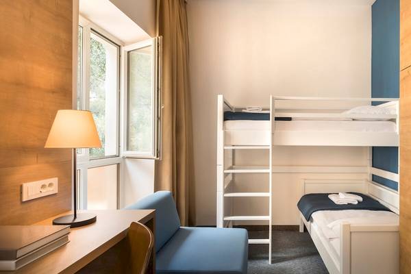 Doppelstockbett-Zimmer im Remisens Hotel Epidaurus mit Lampe, Schrank und Büchern auf dem Schreibtisch.