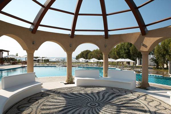 Poolbereich des Lindian Village Beach Resort auf Rhodos mit überdachtem Bereich und weißen Bänken.