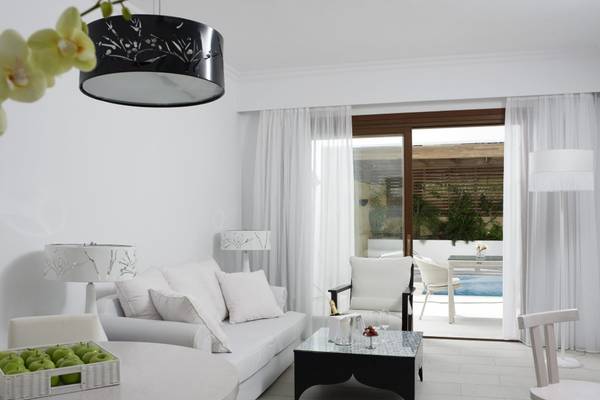 Ein modernes weißes Wohnzimmer im Lindian Village Beach Resort Rhodes mit einem Sofa, einem Tisch und einer Terrasse mit Pool.