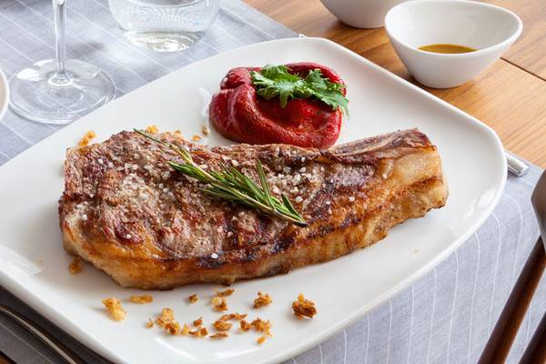 Gegrilltes Steak mit Rosmarin und roter Paprika auf weißem Teller.