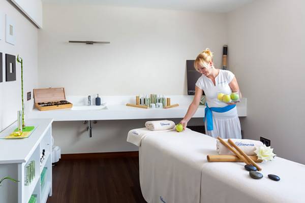 Eine Frau in einem weißen Kleid bereitet einen Massagetisch im Tigotan Lovers & Friends Hotel vor.