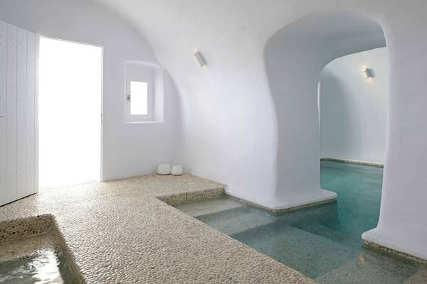 Innenansicht des Badezimmers im Katikies Chromata Hotel auf Santorini mit weißen Wänden und einem kleinen Pool.