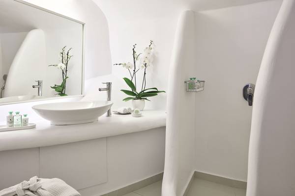 Badezimmer des Katikies Chromata Santorini Hotels mit weißem Waschbecken und Orchideen.