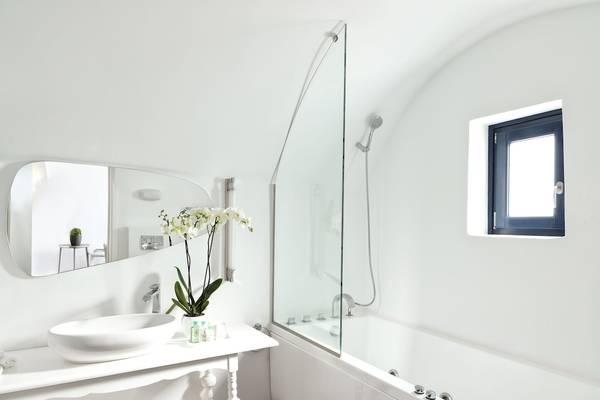 Ein Badezimmer im Katikies Chromata Santorini Hotel mit einer weißen Wanne, einem Waschbecken und einem Spiegel.