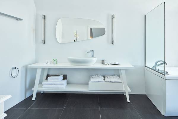 Badezimmer im Katikies Chromata Santorini Hotel mit weißem Waschtisch und Dusche.