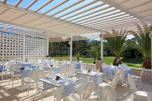 Außenbereich des Mythos Palace Resort & Spa mit blauen und weißen Tischen und Stühlen unter einer Pergola.