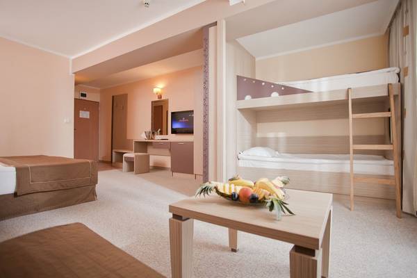 Innenansicht eines Hotelzimmers im DIT Evrika Beach Club mit Doppelbett, Etagenbett und Tisch mit Obst.