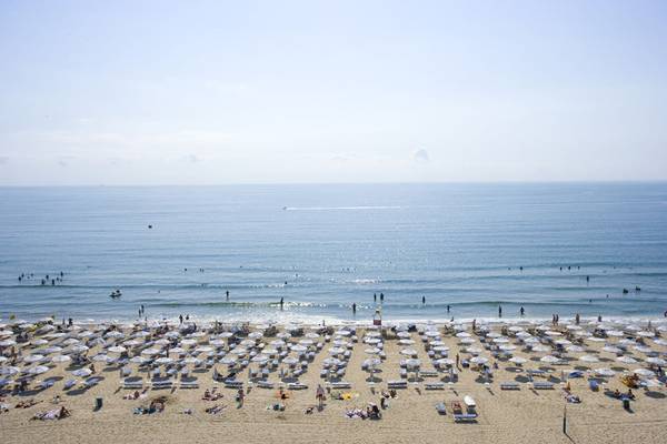 Ein Strand mit vielen Sonnenschirmen und vielen Menschen, die entspannen und schwimmen.