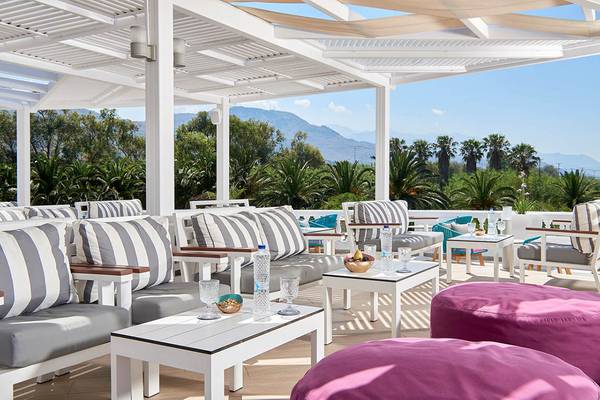 Mythos Palace Resort & Spa Terrasse mit Tischen, Stühlen und Kissen.