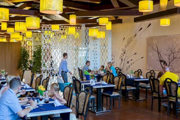 Innenansicht des DIT Evrika Beach Club Restaurants mit Gästen an Tischen und gelben Deckenleuchten.