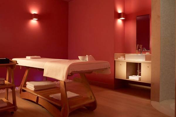 Luxuriöser Spa-Behandlungsraum im Daios Cove Luxury Resort & Villas mit roten Wänden, Massagetisch und blauen Beleuchtungselementen.