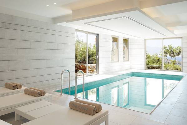 Innenpool des Daios Cove Luxury Resort & Villas mit weißen Sonnenliegen und Ausblick auf die Natur