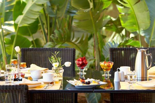 Frühstückstisch im Garten des Daios Cove Luxury Resort & Villas mit Früchten und Kaffeeservice.