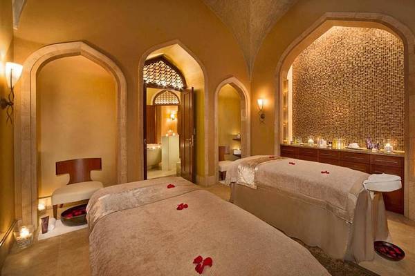 Behandlungsraum im Atlantis The Palm Spa mit zwei Massageliegen, dekorativen roten Rosenblättern und warmem Licht.