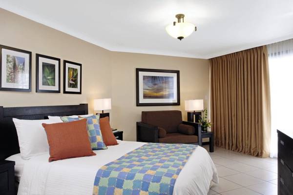 Hotelzimmer im Amsterdam Manor Beach Resort mit einem Bett, Kissen, Lampe und einem Sessel.