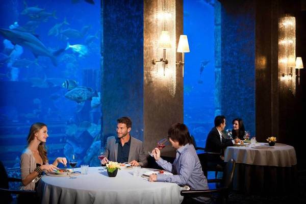 Besucher in einem Restaurant im Atlantis The Palm, das Fenster zeigt einen großen Aquarium.